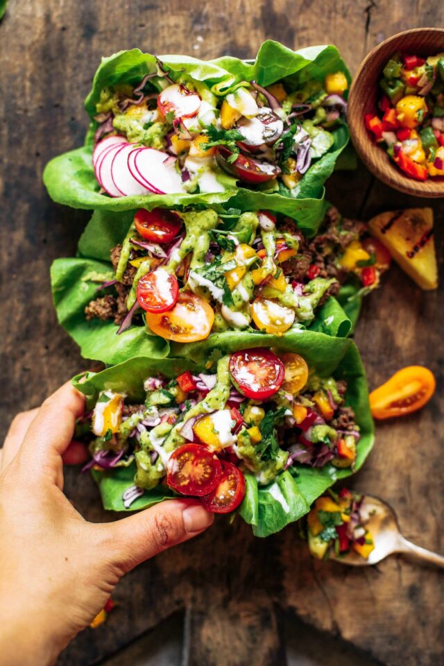 lettuce wrap tacos on a wooden board with a hand holding one