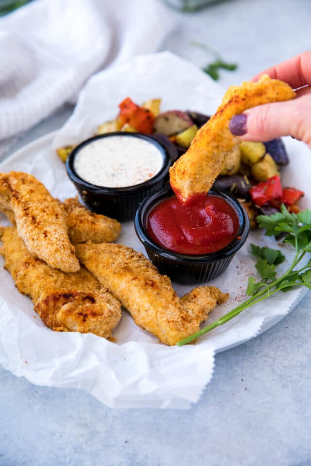 chicken tender being dipped into ketchup and served with a side of roasted veggies