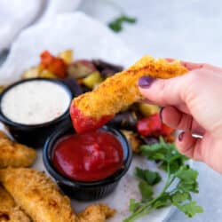 woman's hand holding a chicken tender and dipping it into ketchup