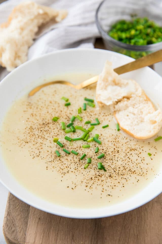 potato soup with bread and a gold spoon served in a white bowl