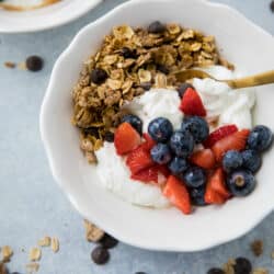 yogurt and granola in a white bowl topped with berries and served with a gold spoon