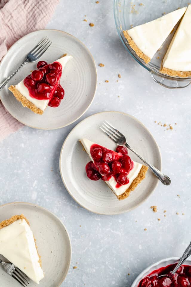 slices of no-bake cheesecake topped with cherries and served on small white plates