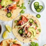 Salmon tacos topped with avocado crema and sliced jalapeño.