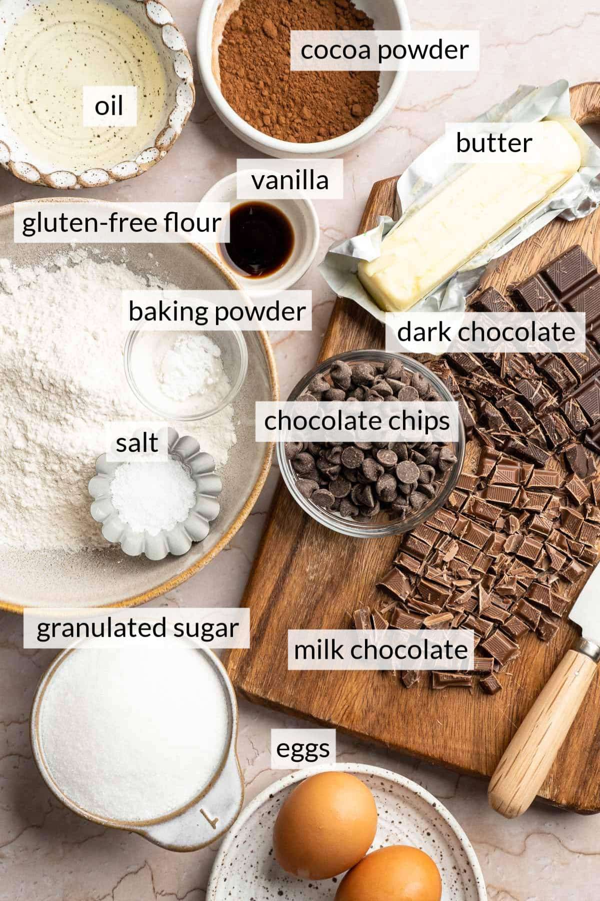 Chopped chocolate near bowls of flour, cocoa powder, sugar and eggs.