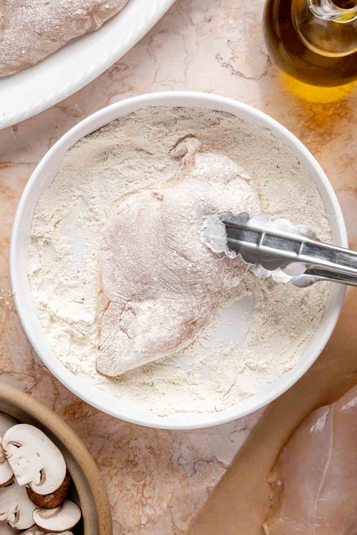 Using tongs to coat chicken in flour.