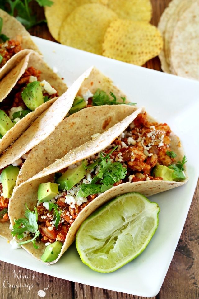 tacos on a white plate topped with avocado and cilantro