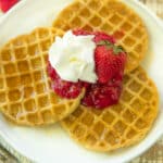 three waffles on a white plate and topped with strawberry sauce and whipped cream