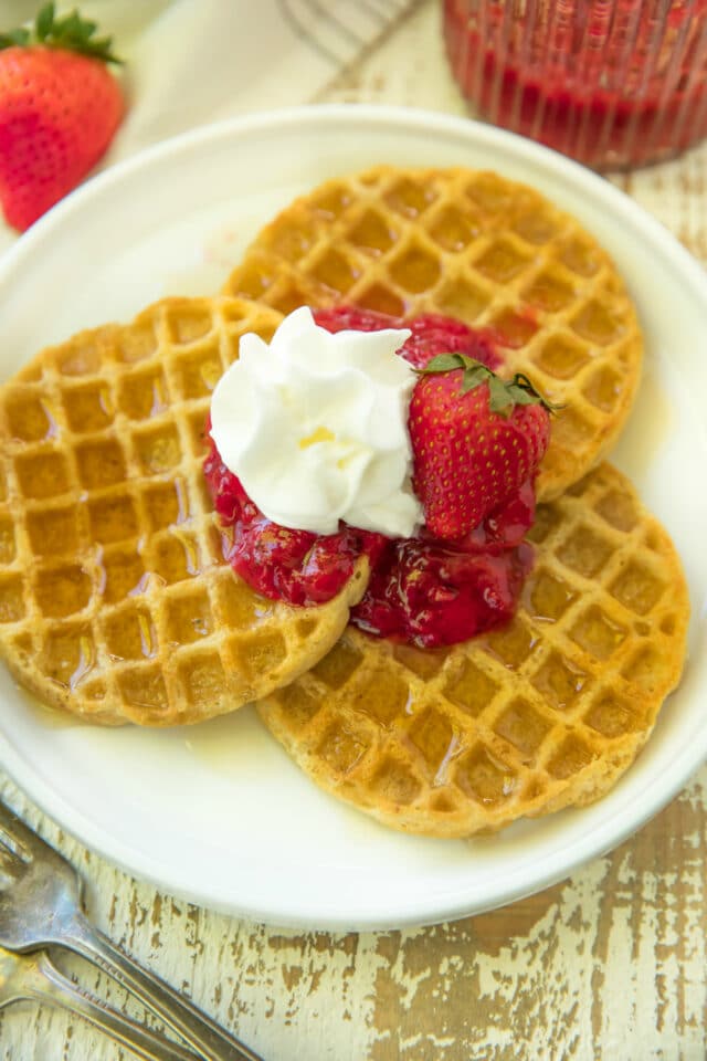 three waffles on a white plate and topped with strawberry sauce and whipped cream