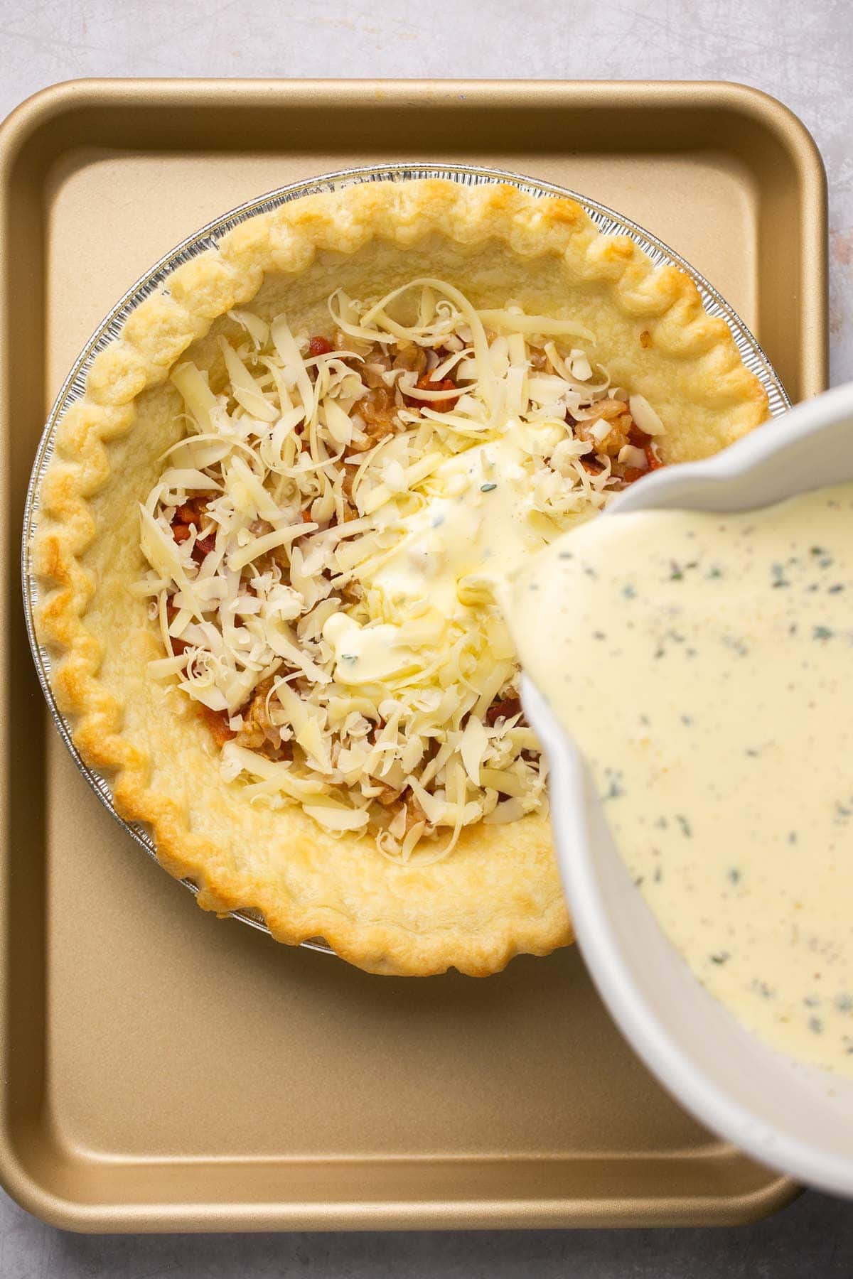 Pouring egg custard over bacon and cheese in a pie crust.