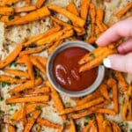 woman's hand dipping sweet potato fries into ketchup