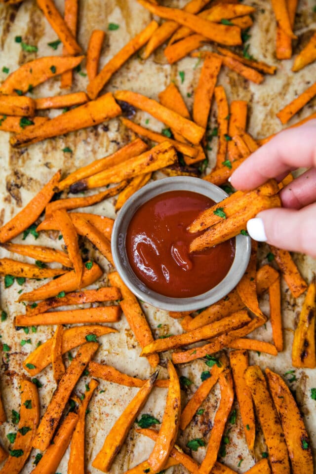 woman's hand dipping sweet potato fries into ketchup
