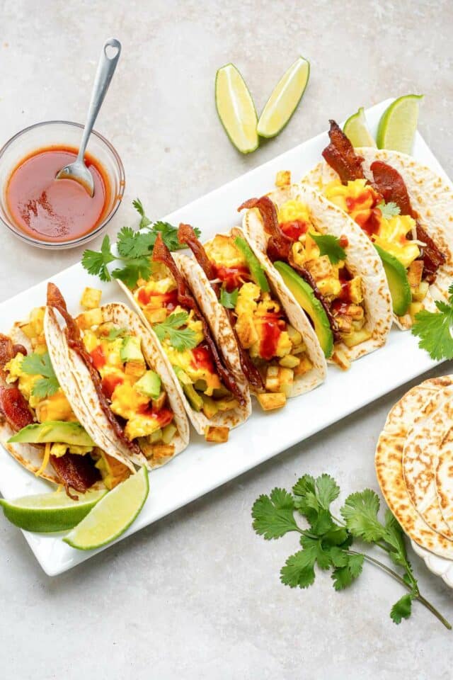 Tacos with scrambled eggs and bacon served with hot sauce.