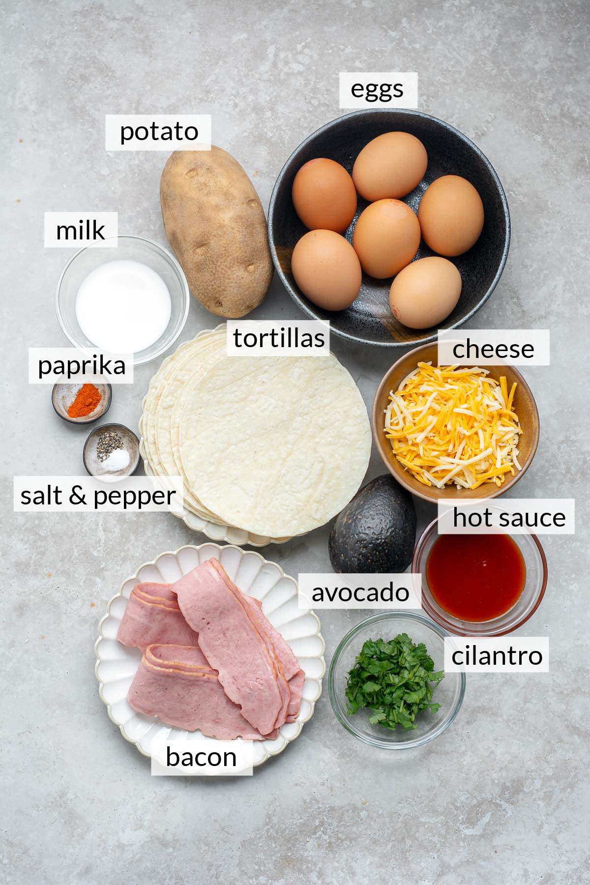 Tortillas near eggs, a potato, bacon, cheese, milk, paprika, salt, pepper and cilantro.
