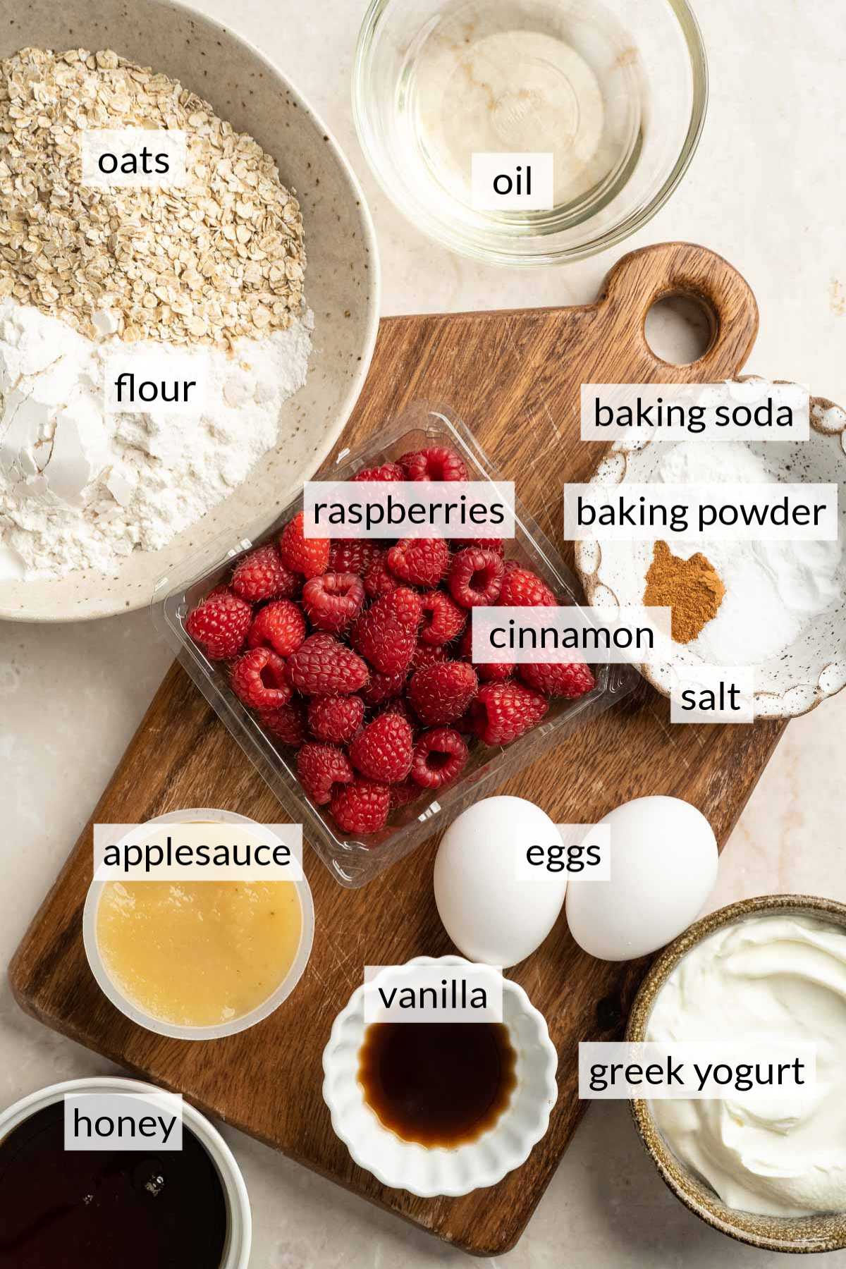 Fresh raspberries near eggs, flour, oats, applesauce, honey, vanilla and greek yogurt.