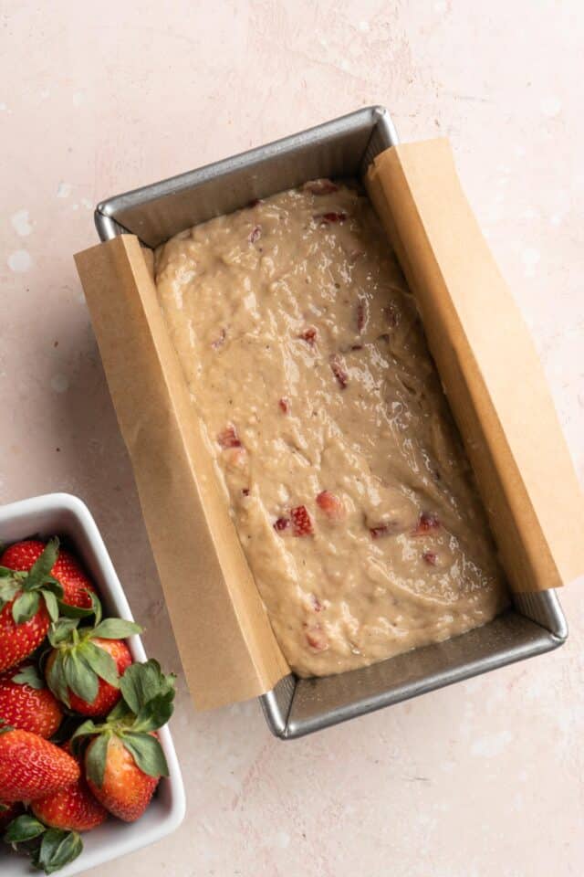 Adding bread batter to a loaf pan lined with parchment paper.