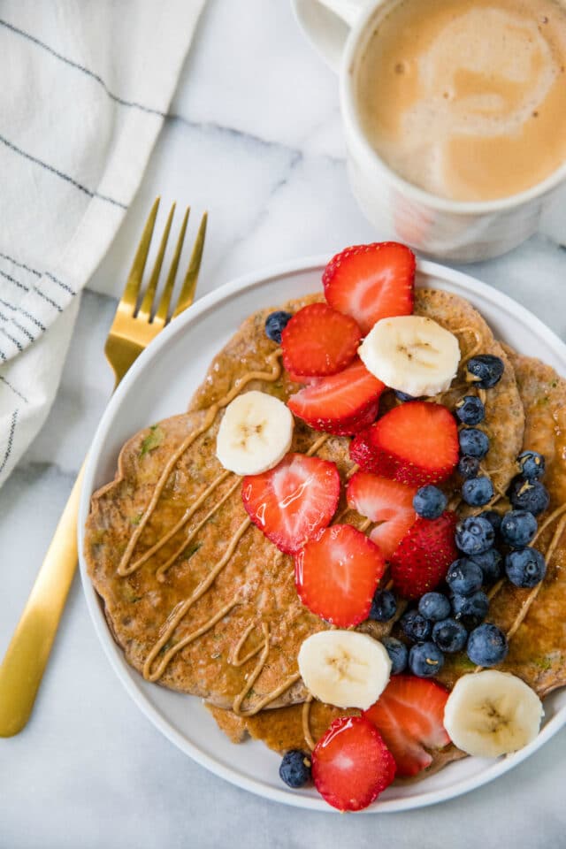 Protein Zucchini Pancakes on a white plate served with a cup of frothy coffee