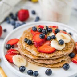 Protein Zucchini Pancakes stacked on a white plate and topped with berries