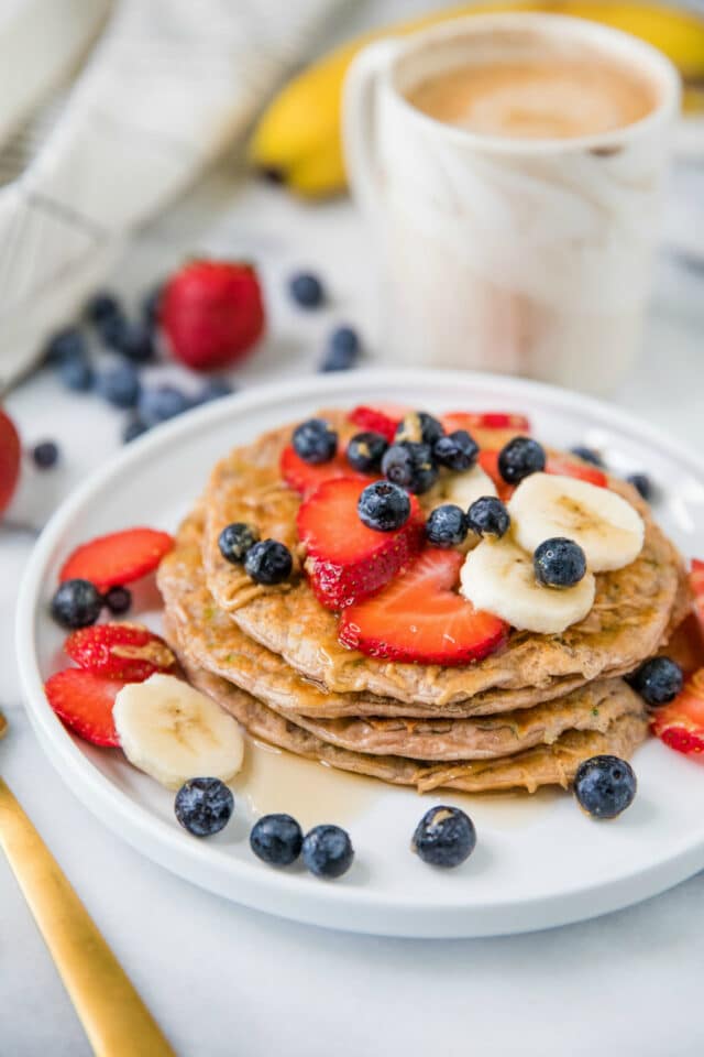 Protein Zucchini Pancakes stacked on a white plate and topped with berries