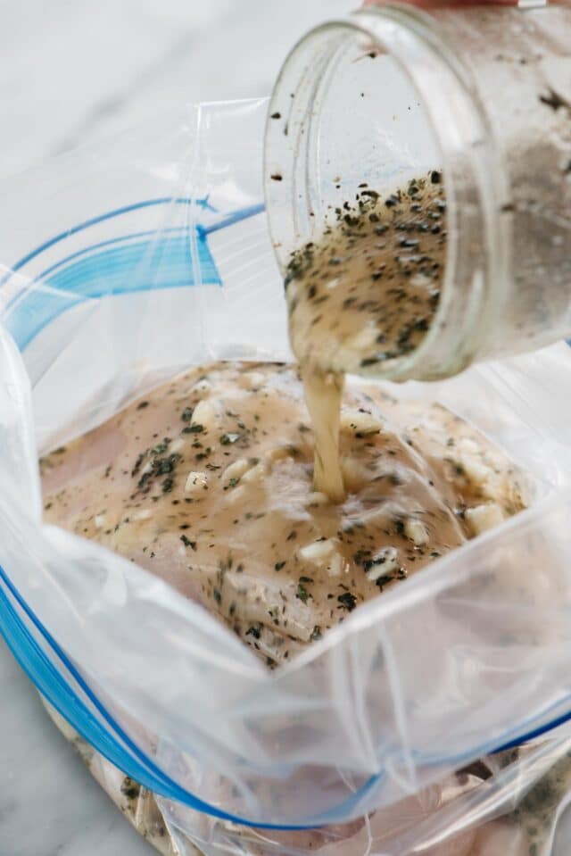 jar of marinade being poured into baggie with chicken
