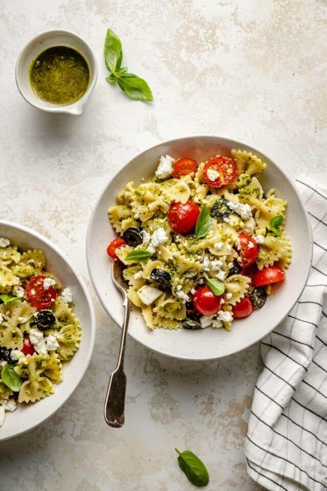 Two white bowls filled with farfalle pasta mixed with basil pesto.