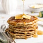 A stack of zucchini pancakes being topped maple syrup.