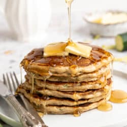 A stack of zucchini pancakes being topped maple syrup.