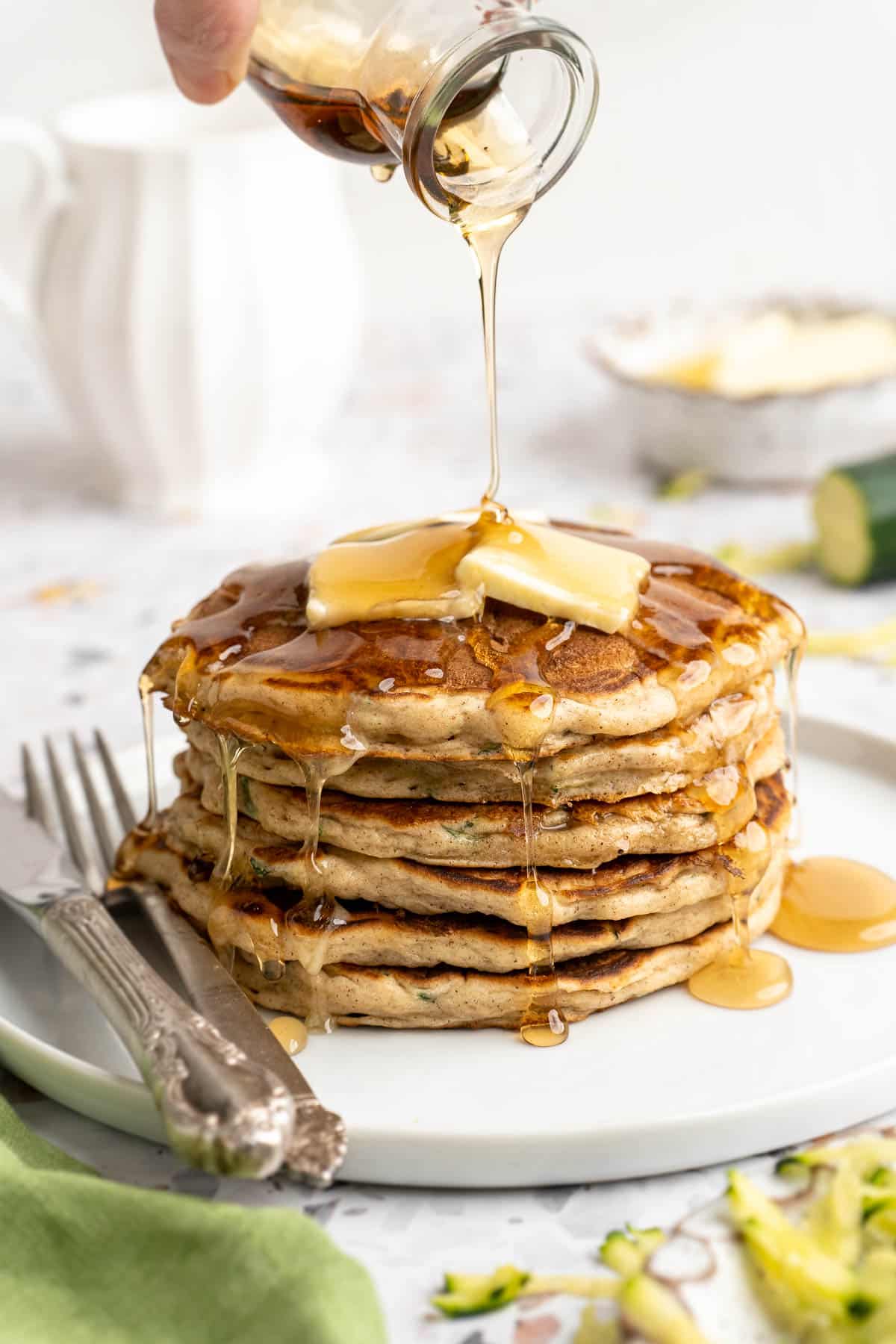 A stack of zucchini pancakes being topped maple syrup.