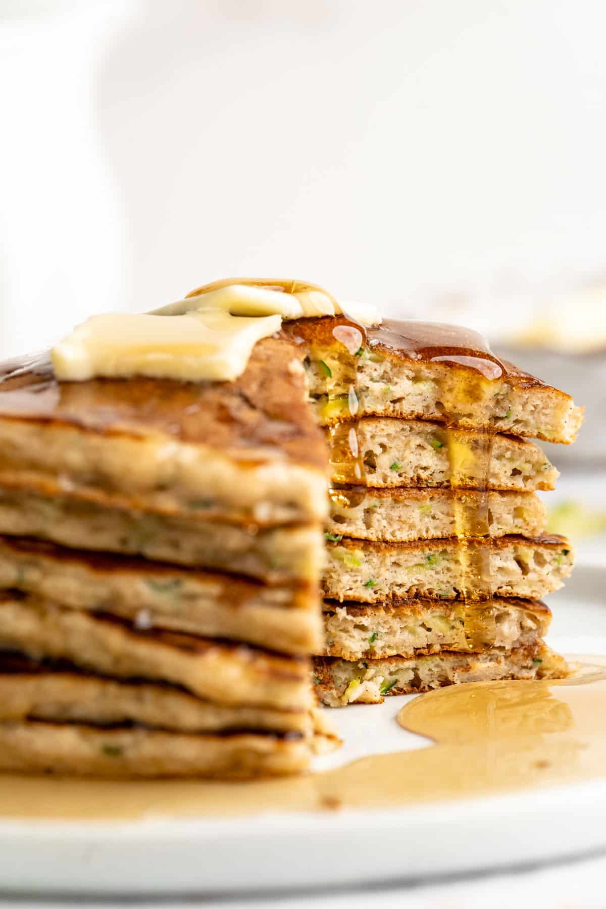 A cut stack of zucchini pancakes with syrup dripping down the inside.