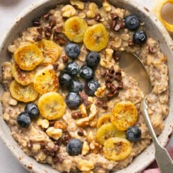 Bowl of banana bread oatmeal topped with sliced banana and blueberries.