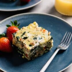 Serving of egg casserole on a blue plate with strawberries and a fork.