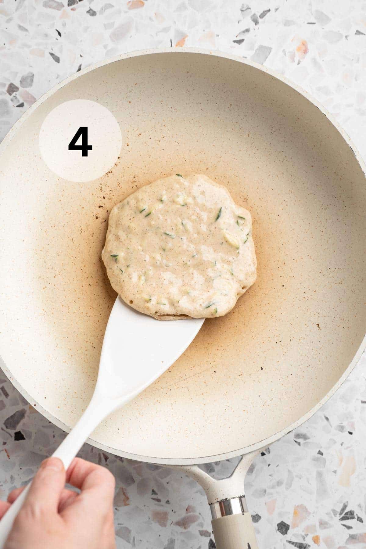 Flipping a zucchini pancake in a skillet.
