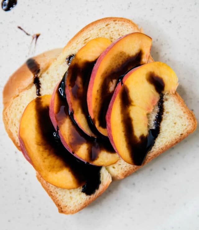 bread topped with sliced peaches and balsamic drizzle on a large skillet