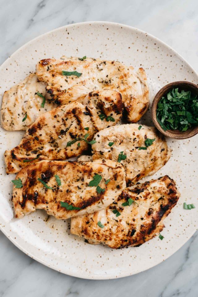grilled chicken breasts on a serving plate garnished with fresh parsley