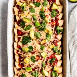 easy chicken enchiladas in a white baking dish topped with avocado and cilantro