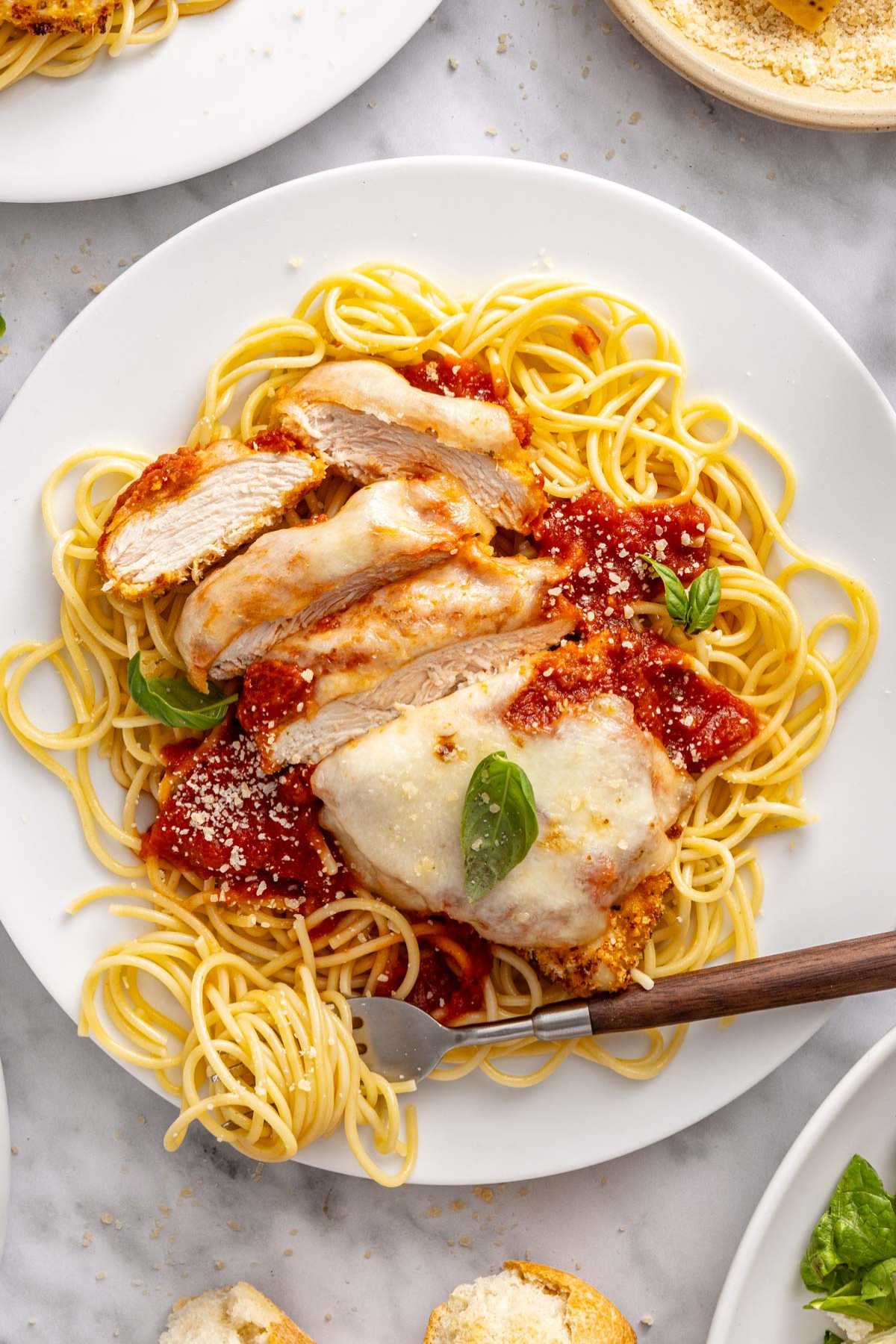 Sliced chicken parmesan over spaghetti on a white plate.