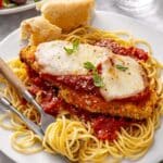 Baked chicken parmesan served over pasta and garnished with fresh basil.