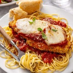 Baked chicken parmesan served over pasta and garnished with fresh basil.