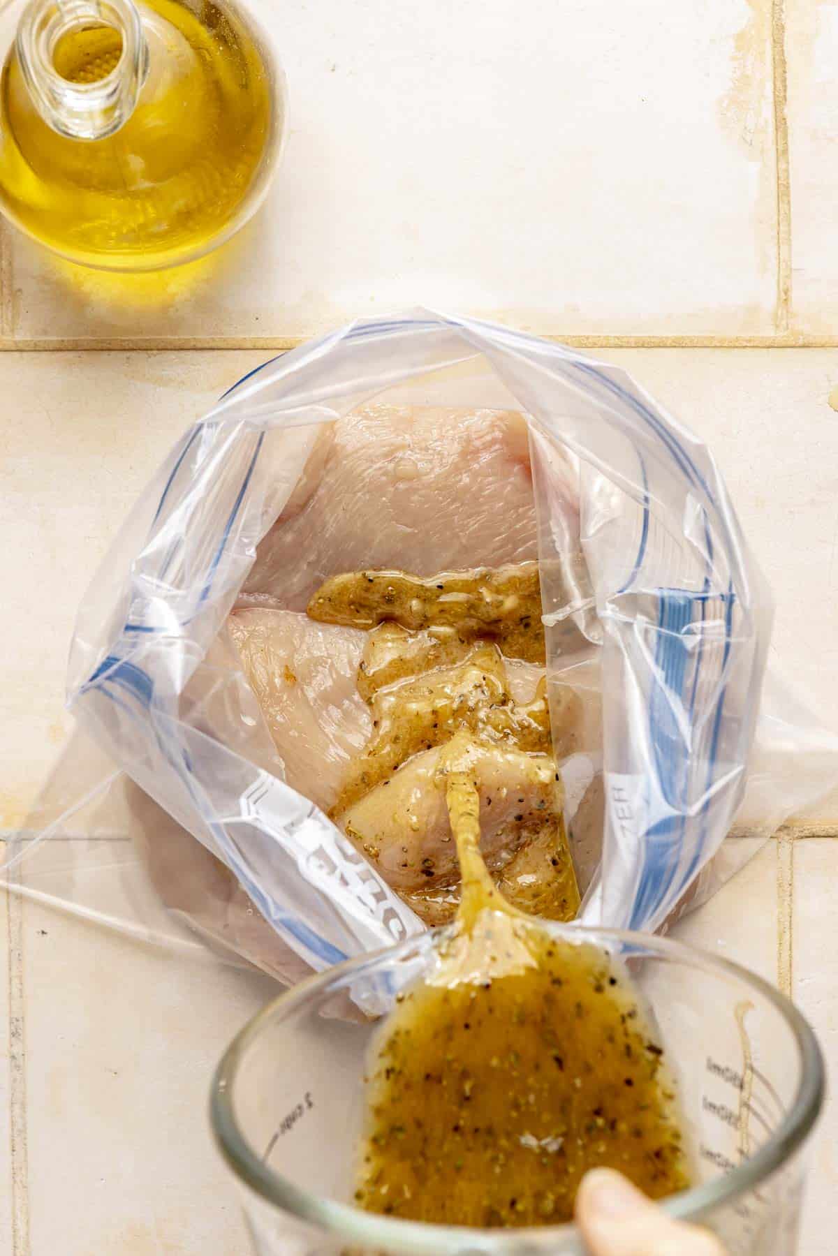 Pouring marinade into a bag with raw chicken breasts.