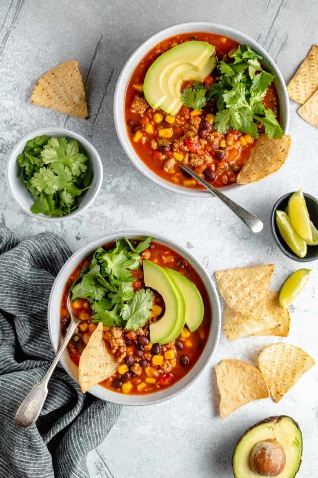 two bowls of taco soup served with tortilla chips and lime wedges