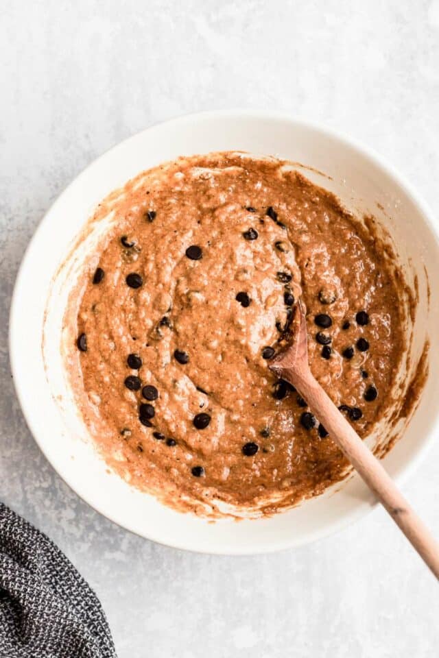 Stirring chocolate chips into muffin batter with a wooden spoon.