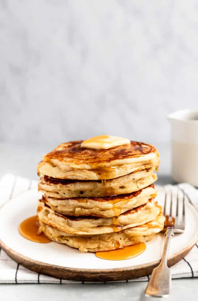 a stack of Buttermilk Pancakes served on a white plate with butter and maple syrup
