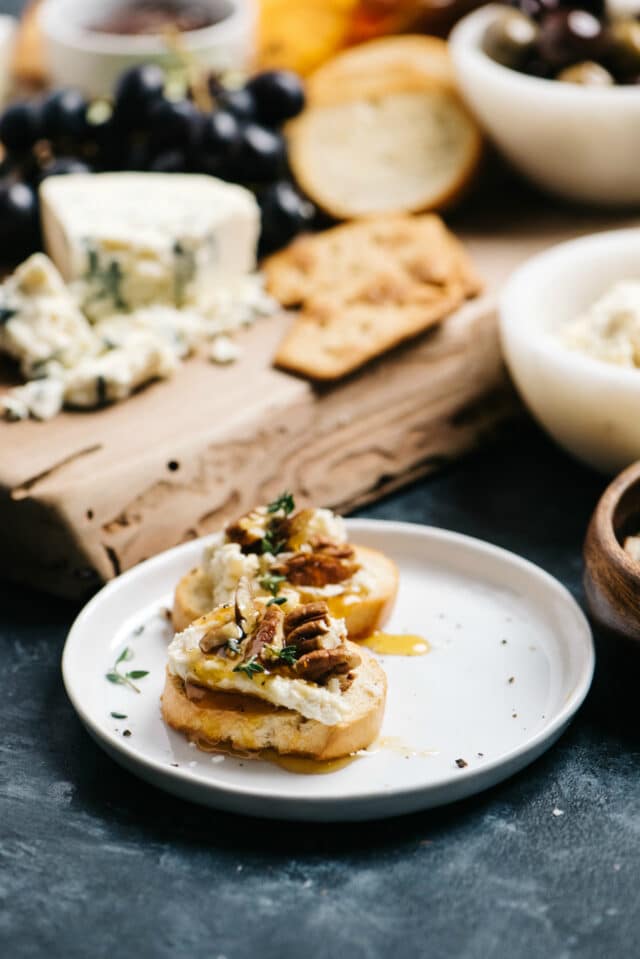 little toasts topped with goat cheese, honey and pecans served near a cheese board