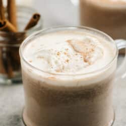 hot cocoa in a glass mug and topped with whipped cream and a sprinkle of cinnamon