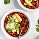 turkey chili in a white bowl and topped with avocado slices, cheese and fresh cilantro