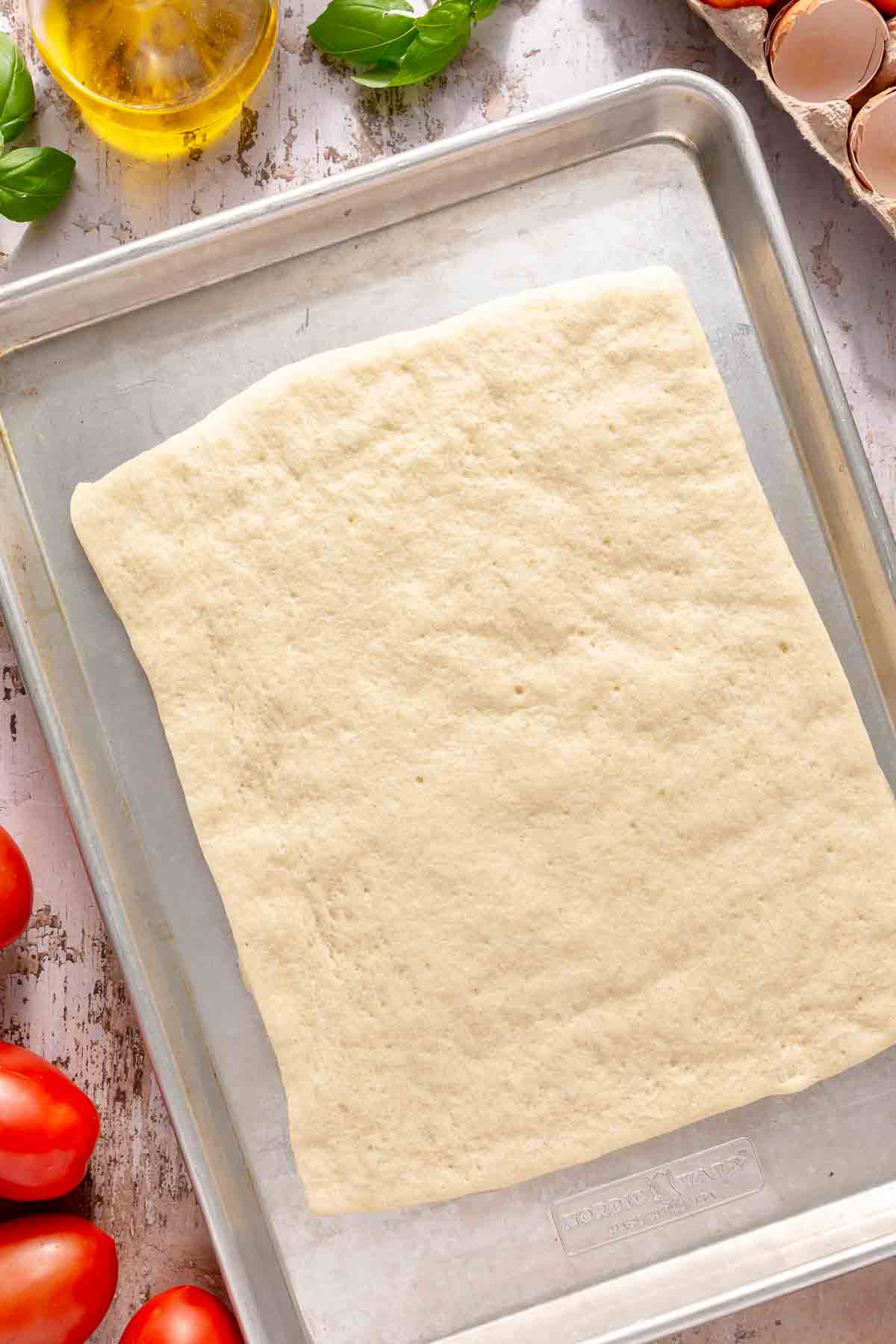 Baked rectangular pizza crust on a sheet pan.