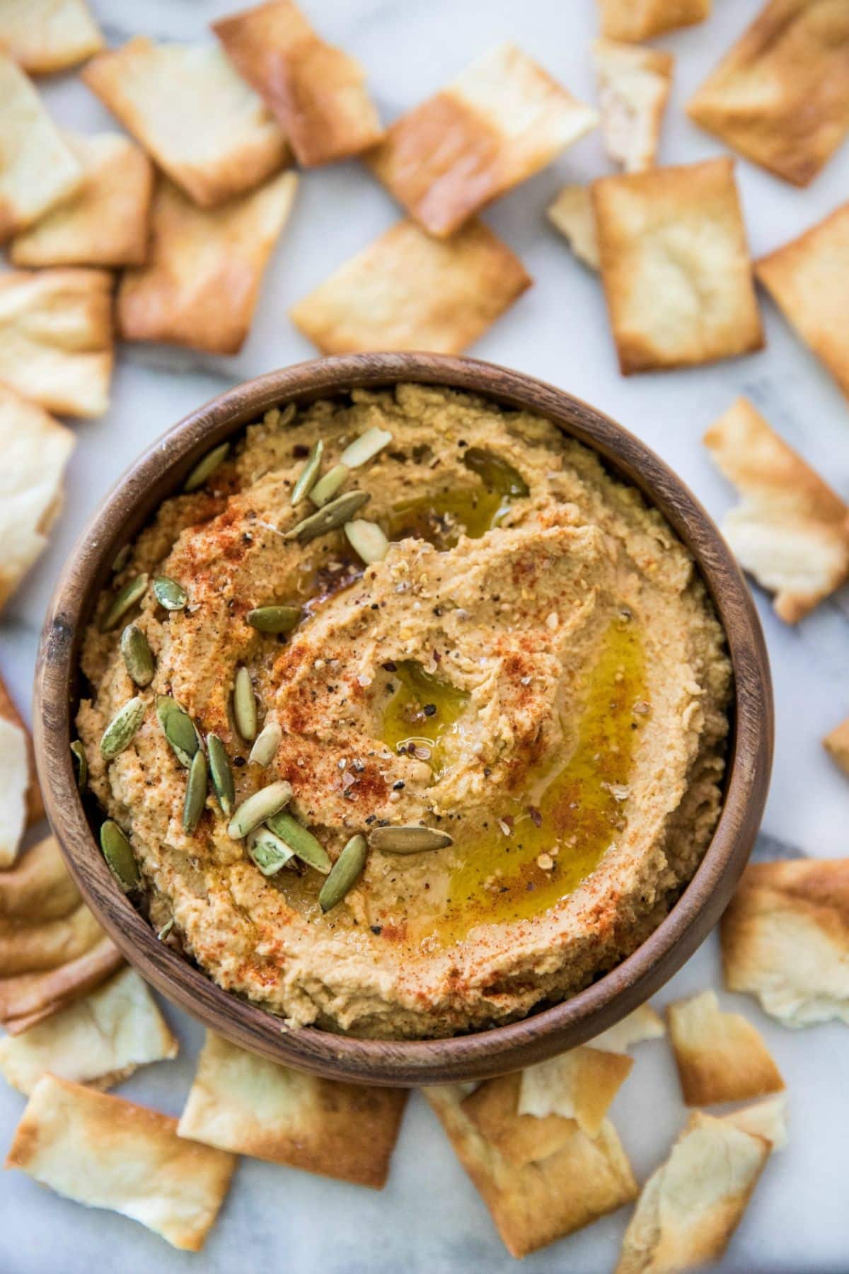 Pumpkin hummus in a bowl topped with pumpkin seeds and surrounded by pita chips. 