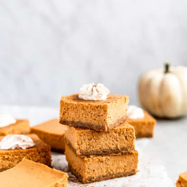 pumpkin cheesecake bars stacked and topped with whipped cream