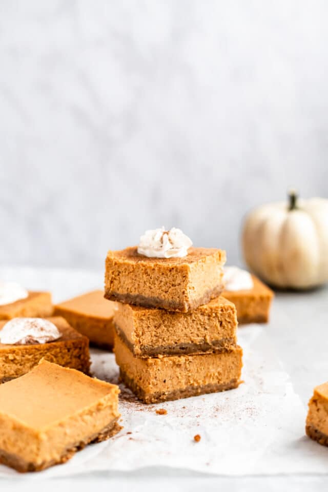 pumpkin cheesecake bars stacked and topped with whipped cream