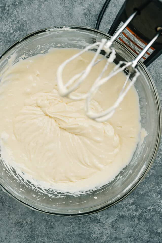 cheesecake filling mixed with an electric mixer in a glass mixing bowl 