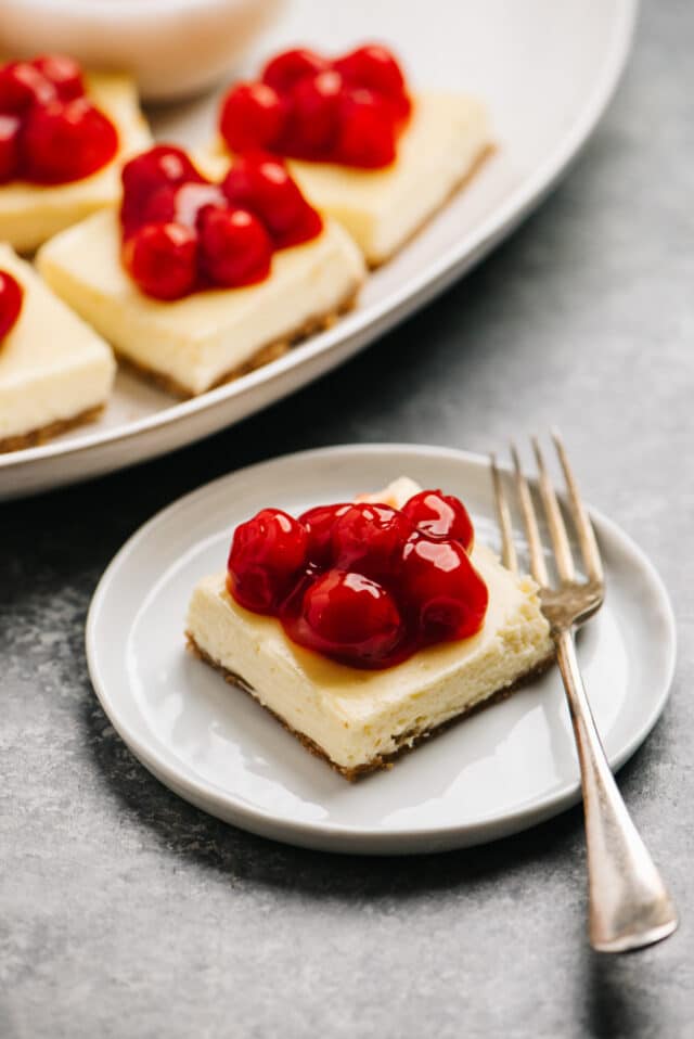 cheesecake bars on a white plate topped with cherries